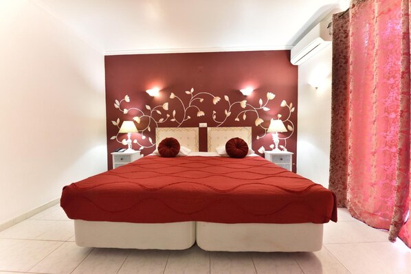 A double bed with a red quilt, two bedside lamps, and a floral wall design. - Hotel Bejense (Beja)