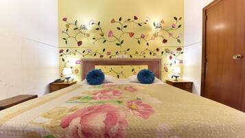 A hotel room with a floral-patterned bedspread, a wooden headboard, and wall-mounted lamps.