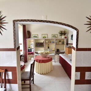 A dining area with a table and chairs, a kitchen area with cabinets and shelves, and a decorative archway. - Hotel Bejense (Beja)