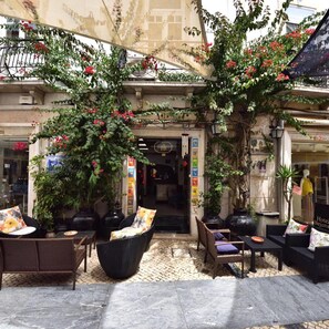 An outdoor seating area with wicker furniture, potted plants, and a building entrance. - Hotel Bejense (Beja)