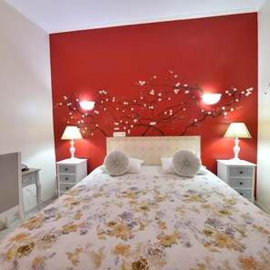 A bedroom with a red wall, a floral bedspread, two nightstands with lamps, and a headboard with a tree design. - Hotel Bejense (Beja)