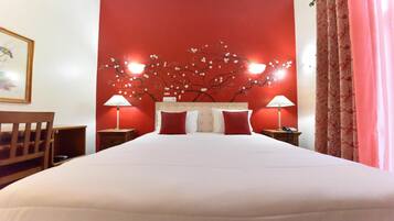 Une chambre d’hôtel avec un grand lit, deux lampes de chevet, un mur rouge orné d’un motif floral et une chaise en bois.