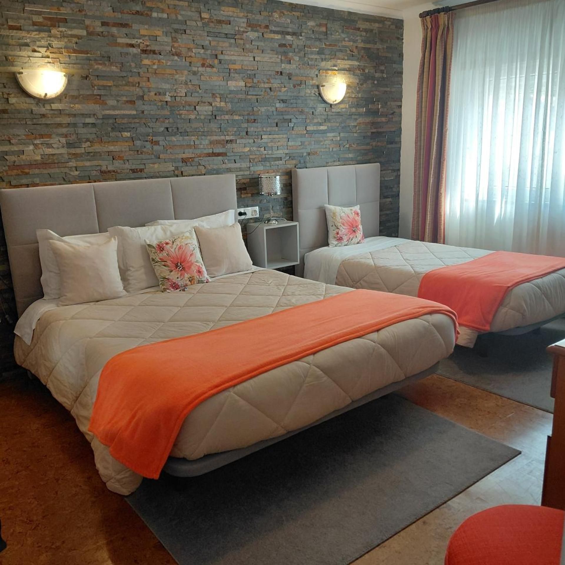 A hotel room with two beds, a brick wall, and a window with curtains.