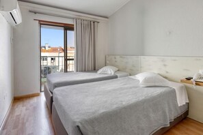 Une chambre d’hôtel avec deux lits, un balcon, un téléphone sur une table de chevet et une fenêtre avec des rideaux.