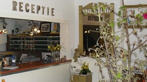 A reception area with a wooden counter, a mirror, a plant, and a sign that reads 'RECEPTION'. - Hotel Hoogland Zandvoort Aan Zee (Zandvoort)