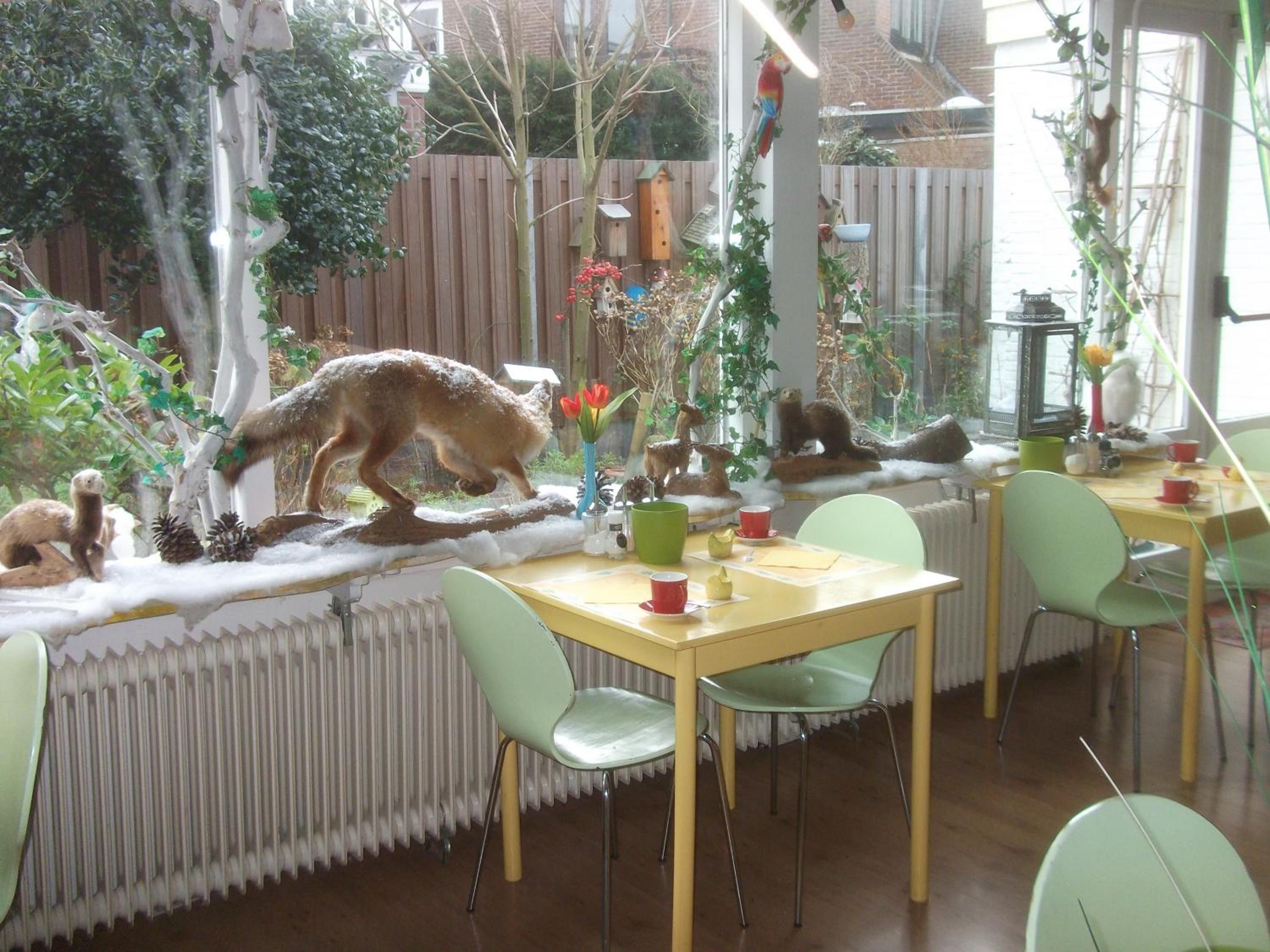 Een eethoek met een tafel, stoelen, een radiator en een raam met uitzicht op een tuin.