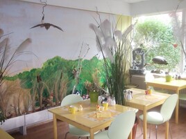 A room with a mural of a forest scene, a dining table with chairs, and a window with a view of trees.