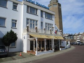 A hotel with a white facade, a balcony with flags, and a tower.