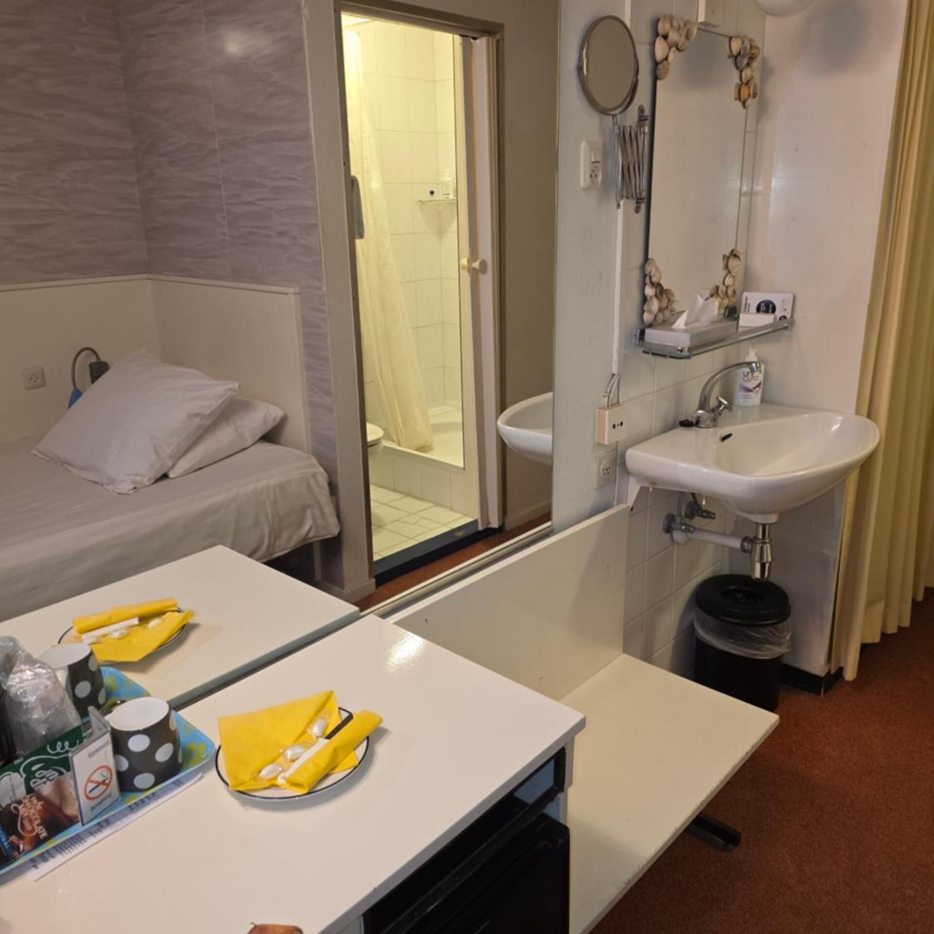 Een hotelkamer met een bed, een badkamer met een wastafel en spiegel, en een tafel met toiletartikelen.