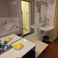 Una habitación de hotel con una cama, un baño con lavamanos y espejo, y una mesa con artículos de aseo.
