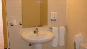 A bathroom with a sink, mirror, lights, towel rack, toilet, and a trash can. - Hotel Gameiro (Entroncamento)