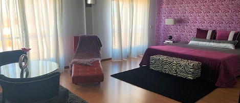 A bedroom with a bed, a chair, a table, and a TV.