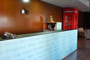 A reception desk with a wooden backdrop, a red telephone booth, and a golden statue. - Hotel Gameiro (Entroncamento)