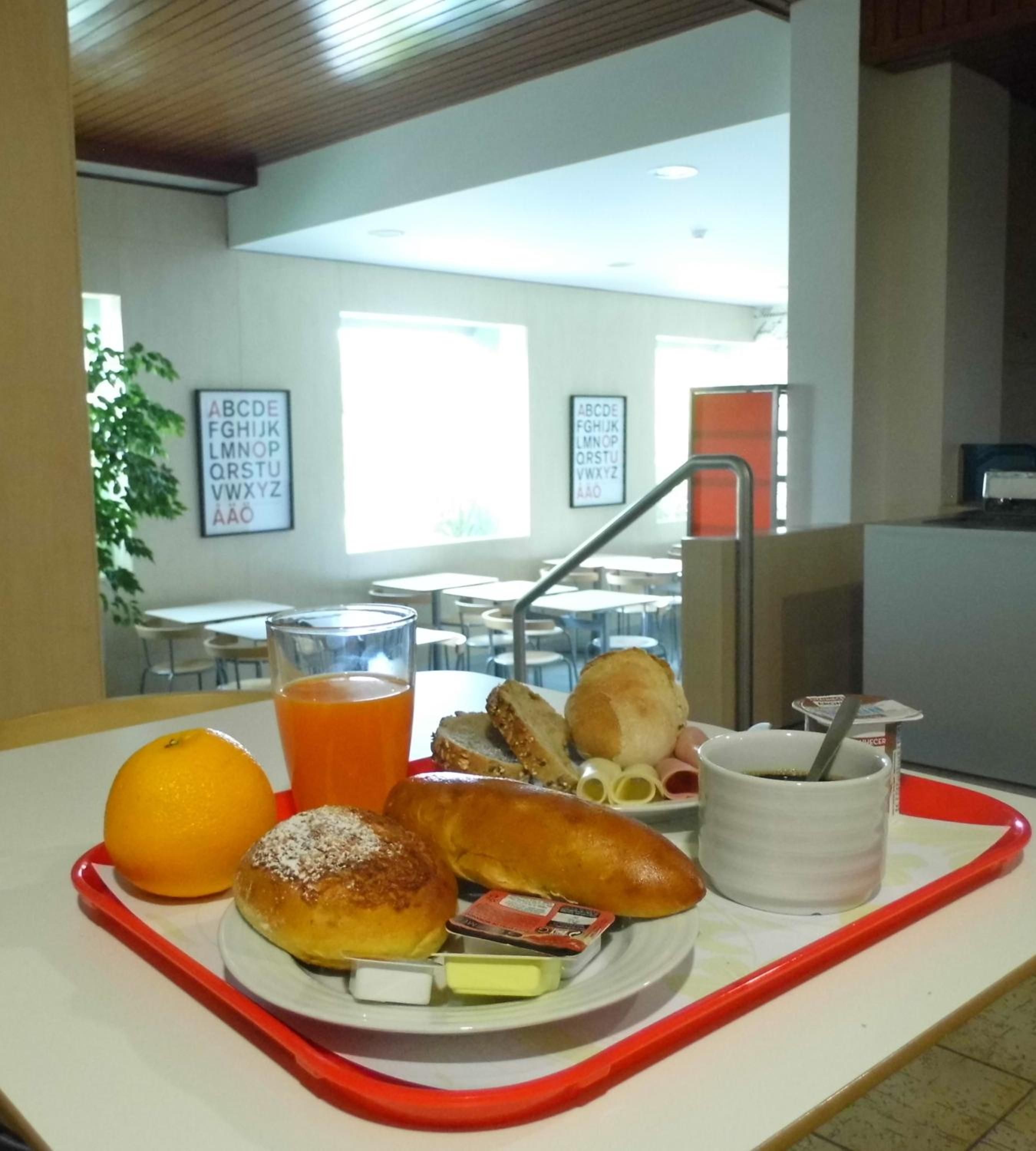 Una bandeja con alimentos para el desayuno, incluyendo pan, una naranja, jugo y una taza.