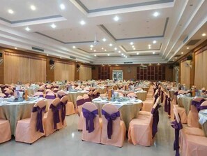 Ein großer Festsaal mit runden Tischen, weißen Tischdecken und Stühlen mit violetten Bändern.