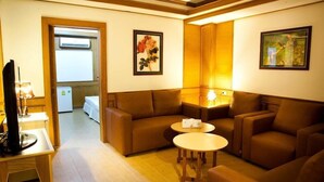 A cozy living room with a brown sofa set, two small round tables, and framed artwork on the walls. - Zaza Hotel (Samut Prakan)