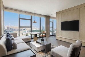 Ein modernes Wohnzimmer mit großem Fernseher, bequemen Sitzmöglichkeiten und Blick auf eine Stadtlandschaft.