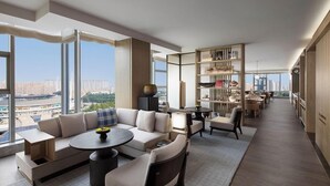A modern living room with a sofa, coffee table, and dining area, large windows with a city view, and a bookshelf. - Courtyard by Marriott Luoyang (Luoyang)