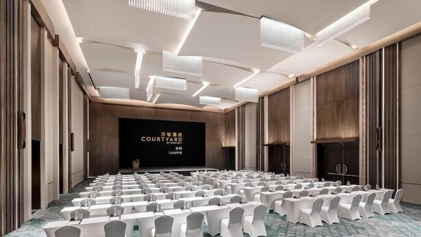 A conference room with rows of tables and chairs, a large screen displaying text, and a patterned carpet. - Courtyard by Marriott Luoyang (Luoyang)