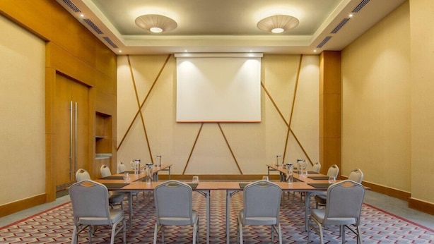 Ett konferensrum med ett stort bord, sex stolar, en projektorduk och en mönstrad matta.