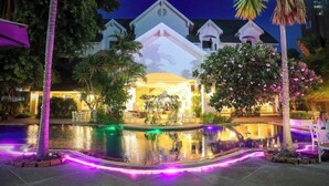 A hotel with a pool, palm trees, and a lit-up building facade. - Pooh Beach Resort and Spa (Pattaya)
