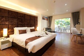 A hotel room with a large bed, a nightstand, a desk, and a view of the outdoors. - Pooh Beach Resort and Spa (Pattaya)