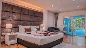 Une chambre moderne avec un grand lit, deux tables de chevet, une tête de lit et une vue sur un jardin tropical, visible à travers une porte vitrée.