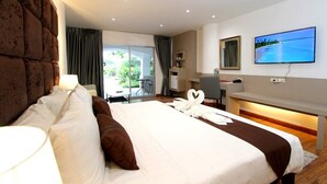 A hotel room with a large bed, a desk, a television, and a view of the outdoors. - Pooh Beach Resort and Spa (Pattaya)