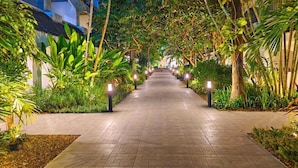 A pathway lined with tropical plants and trees, leading to a building with a modern design. - Pooh Beach Resort and Spa (Pattaya)