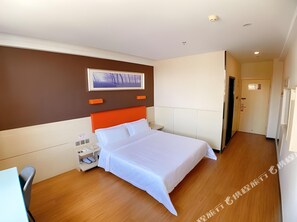 Una habitación de hotel con cama, mesita de noche, un cuadro colgado en la pared y una puerta.