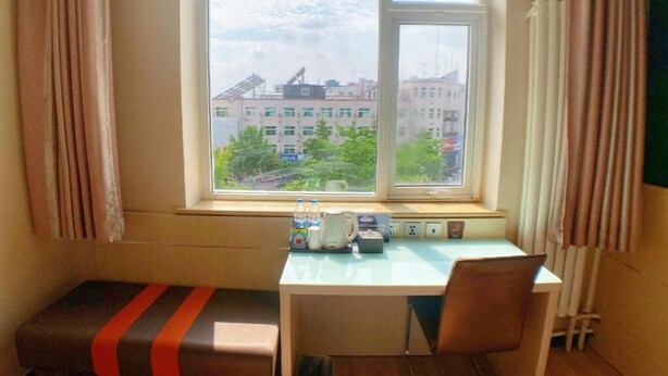A room with a desk, two chairs, a bench, a window with a view of buildings, and a radiator. - 7 Days Premium Beijing Changping Subway Station (Changping)