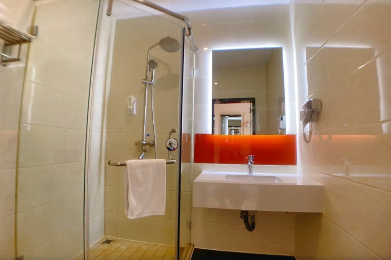 Et moderne badeværelse med glasbrusekabine, hvid vask og spejl med en orange farvet væg.