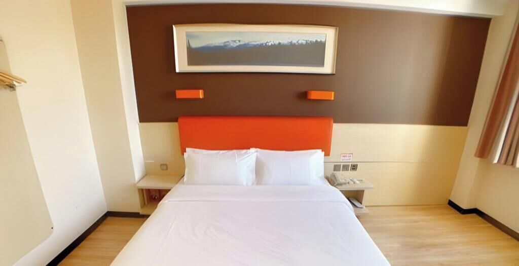 A hotel room with a bed, a nightstand, a telephone, and a painting on the wall.