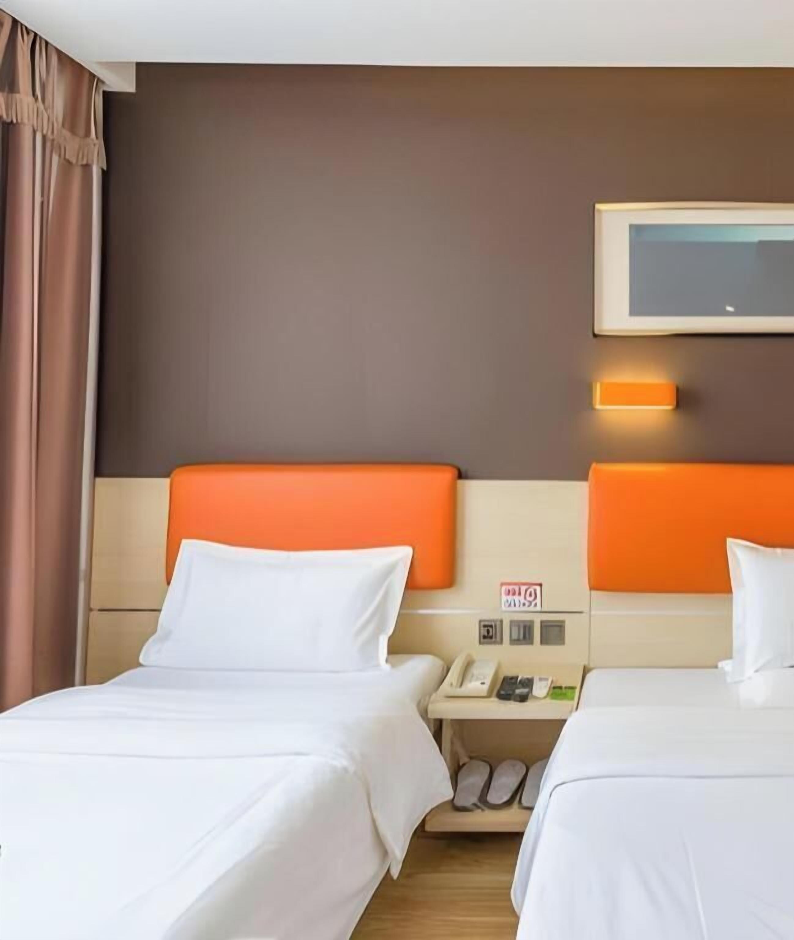 A hotel room with two beds, a nightstand with a phone, and a wall-mounted TV.
