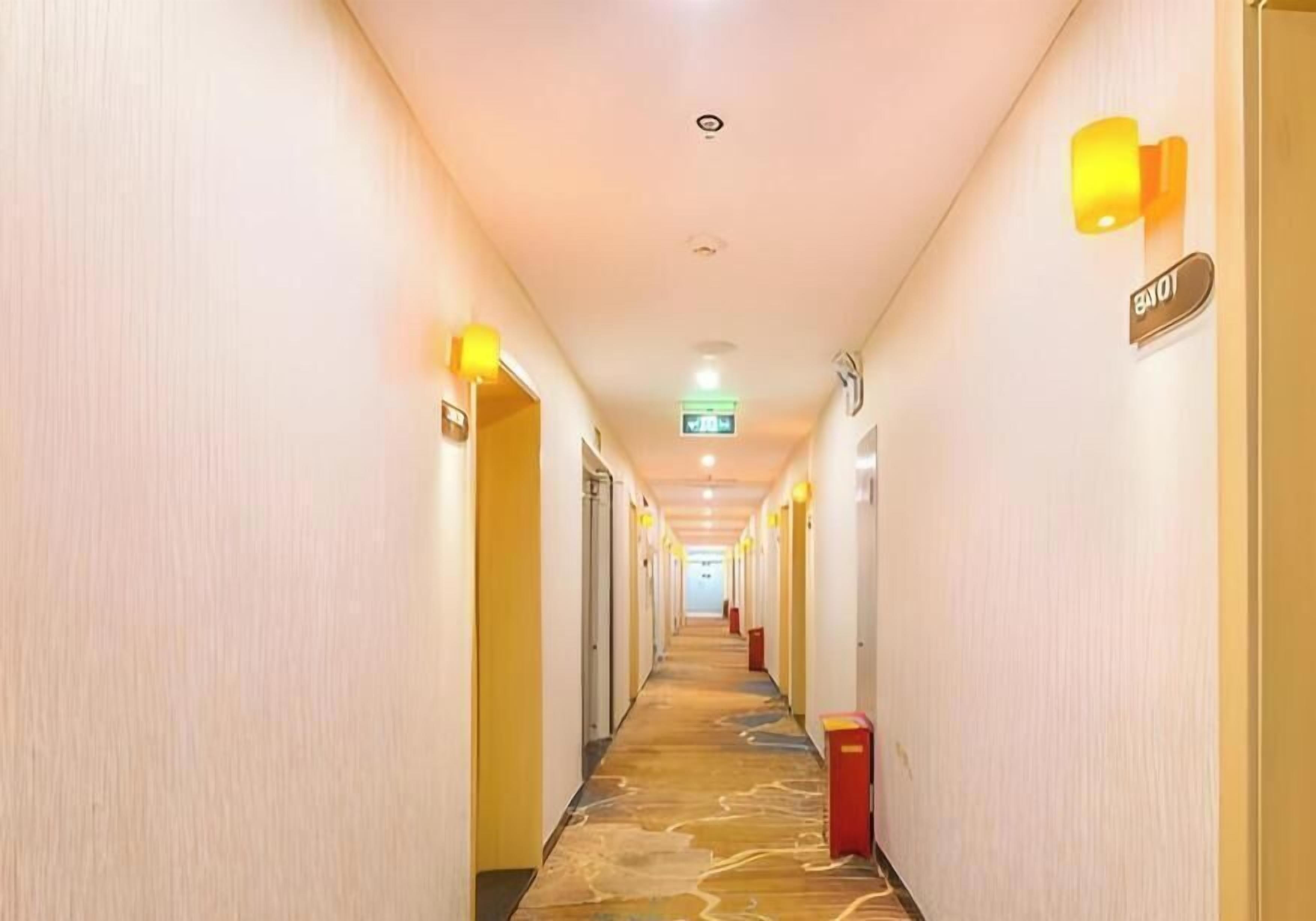 A hotel hallway with a carpeted floor, doors on both sides, and a sign indicating the direction to the elevator.