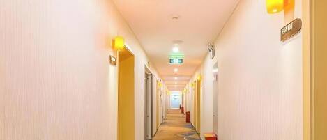 A hotel hallway with a carpeted floor, doors on both sides, and a sign indicating the direction to the elevator.