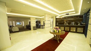 A hotel lobby with a marble floor, a red carpet, a reception desk, and a wall-mounted TV. - Rest Night Serviced Apartments Wadi Al Dawasir (Wadi-Ad-Dawasir)