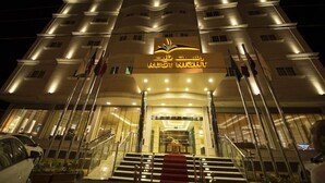 A hotel entrance with a prominent 'REST NIGHT' sign, multiple flags, and a grand staircase leading to the lobby. - Rest Night Serviced Apartments Wadi Al Dawasir (Wadi-Ad-Dawasir)