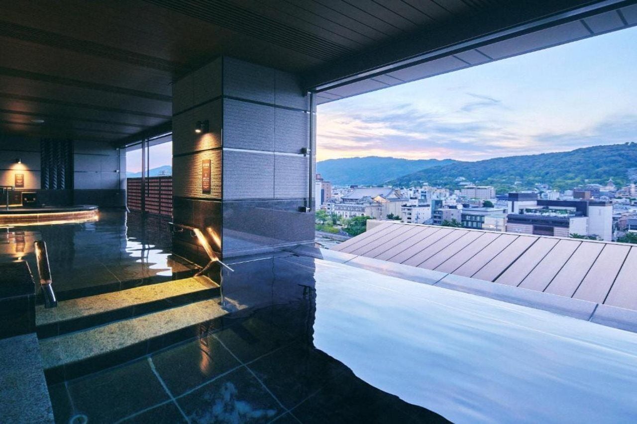 A modern hotel room with a large window overlooking a cityscape and mountains.