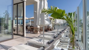 A rooftop lounge with sun loungers, white umbrellas, and a glass balustrade overlooking a cityscape. - Ethereal White Resort Hotel & Spa Adults Only 16+ (Heraklion)
