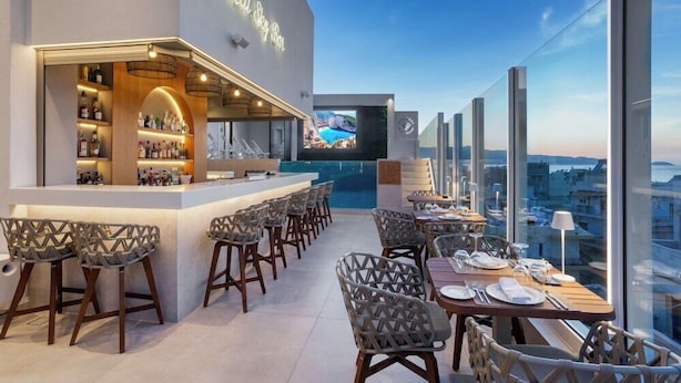A rooftop bar with a bar counter, seating area, and a large screen displaying a scenic view. - Ethereal White Resort Hotel & Spa Adults Only 16+ (Heraklion)