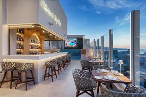 A rooftop bar with a bar counter, seating area, and a large screen displaying a scenic view. - Ethereal White Resort Hotel & Spa Adults Only 16+ (Heraklion)