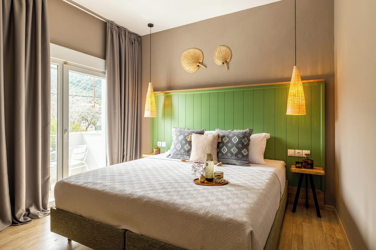 A bedroom with a large bed, green headboard, two wall-mounted lamps, and a small bedside table with a plant.