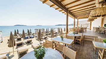 Ein Restaurant am Strand mit Außenbereich, Tischen und Sonnenschirmen mit Blick auf das Meer.