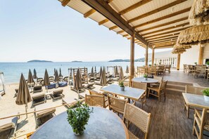 A beachside restaurant with outdoor seating, tables, and umbrellas, overlooking the sea. - Skiathos Theros (Skiathos)