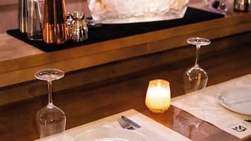 Un espace bar avec un comptoir en bois, un récipient en verre contenant des bouteilles, des verres et une bougie.