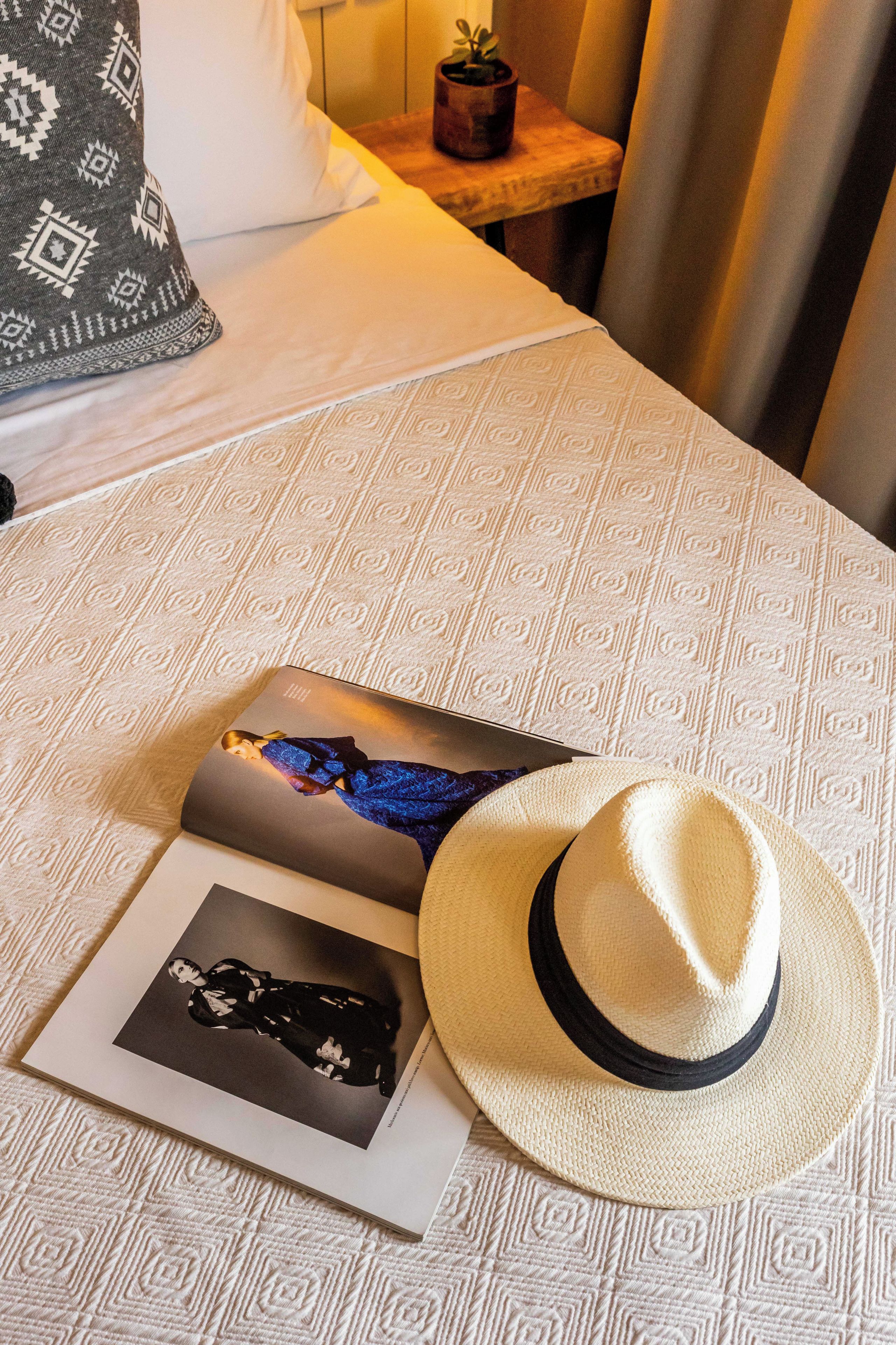 Un lit avec une couvre-lit à motifs, un chapeau et deux magazines posés dessus.