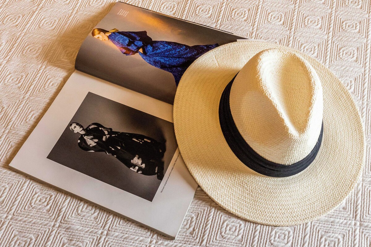 A bed with a patterned bedspread, a hat, and two magazines on it.
