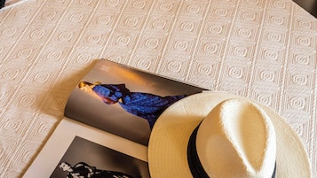 Un lit avec une couvre-lit à motifs, un chapeau et deux magazines posés dessus.