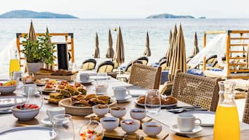 Ein Frühstückstisch mit verschiedenen Speisen, Getränken und Blick auf das Meer.
